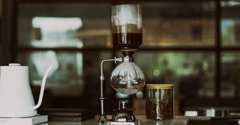 Coffee Maker - A coffee maker on a table with a cup and a glass
